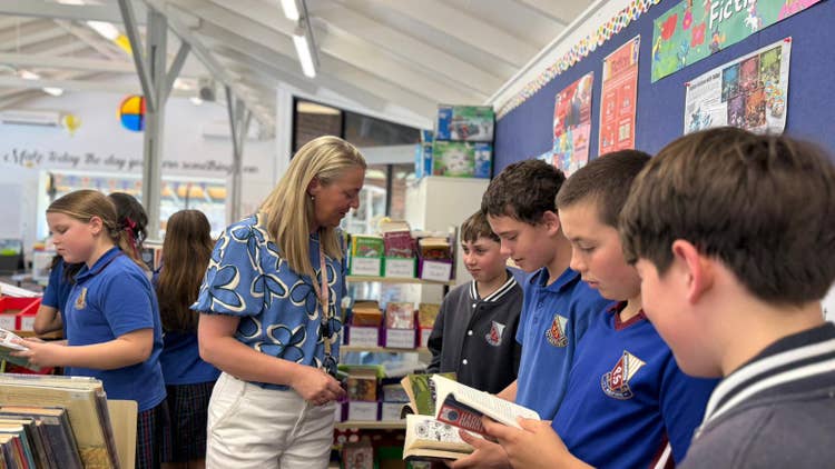 Photo of Year 6 male and female students selecting books in library guided by female library teacher
