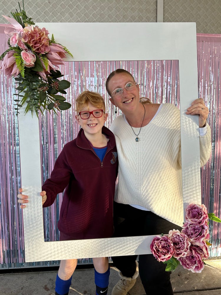 Year 5 male student and mother holding large frame decorated with flowers for photograph