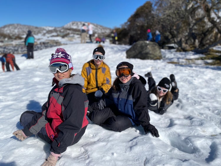 Year 6 male and female students wearing snow gear and googles sitting on snow