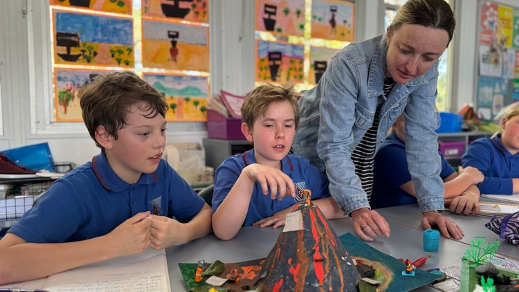 Photo of 2 male Year 4 students and female teacher talking about the volcano model they are making