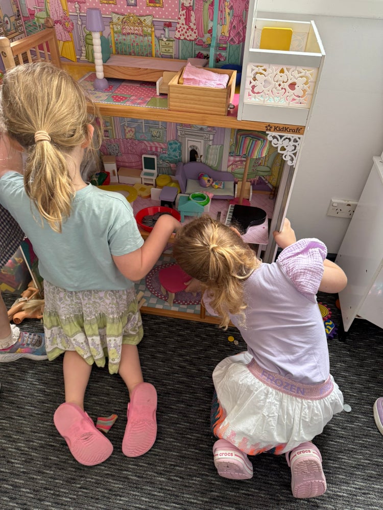 Photo of 2 female preschool students playing with dolls house