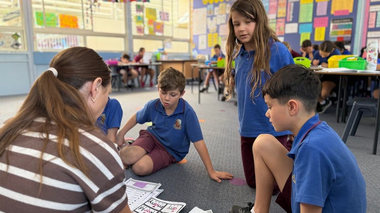 Photo of small group of male and female Year 3 students sitting on the floor with female teacher