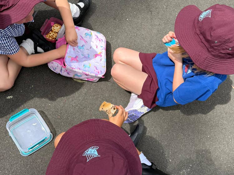Photo of kindergarten female students sitting eating from their lunch box